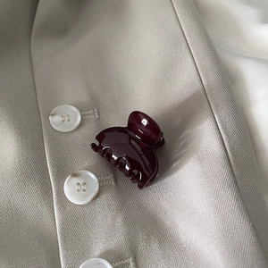 Close-up of a glossy deep burgundy mini hair claw clip placed on a beige blazer fabric
