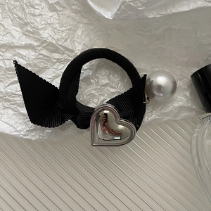 Dettaglio di elastico nero con fiocco, cuore in metallo argento e perla bianca