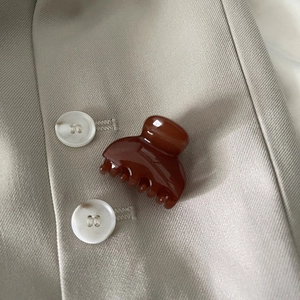 Macro detail of glossy amber brown mini hair claw clip on beige fabric texture
