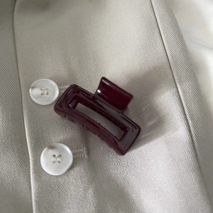 Detail view of a glossy burgundy rectangular hair claw clip on beige fabric background