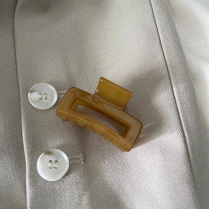 Caramel amber hair claw clip with marble texture on beige blazer pocket background