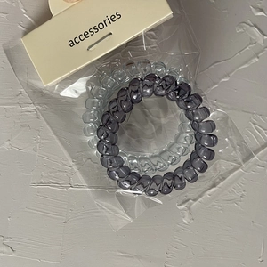 Dettaglio di elastici per capelli a spirale trasparenti e grigio fumo con confezione card
