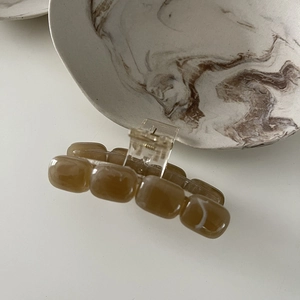 Macro detail of amber marble texture acrylic hair claw clip on a ceramic tray