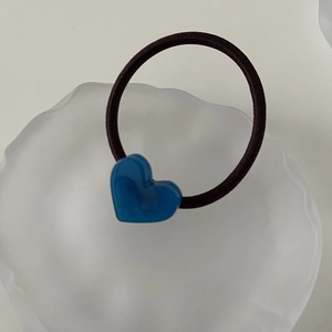 Close-up of a blue resin heart charm on a black elastic hair tie in a white tray