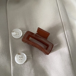 Detail of elegant caramel brown hair claw clip on beige fabric with a sleek hollow design