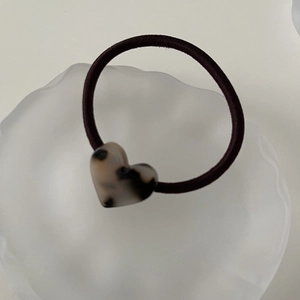 Detail of a minimalist hair tie with a tortoiseshell heart charm on a white tray
