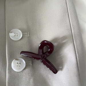 Detail view of burgundy glossy twisted hair claw clip on beige blazer fabric background