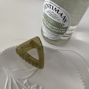 Close-up of olive green triangular resin hair claw clip on a textured white ceramic tray