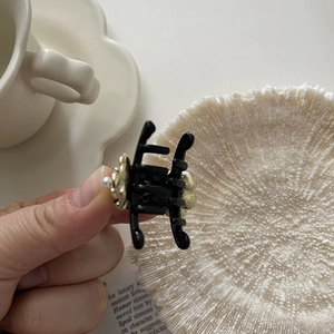 Detail view of mini black hair claw clip featuring golden floral charms and white pearl