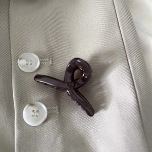 Detail of a glossy dark coffee cross claw clip pinned on a beige fabric jacket collar