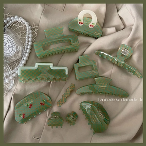 Detail view of green checkerboard acetate hair claws with cherry motifs and wave clip