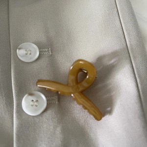 Detail of amber acetate mini hair claw clip clipped onto a beige shirt with buttons