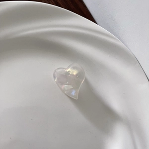 Macro detail of heart-shaped acetate hair clip with iridescent pearl finish in a ceramic bowl