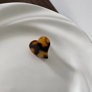 Detail of a mini heart hair claw clip with classic tortoiseshell texture on a white plate