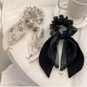 Close-up of chiffon ribbon scrunchies with elegant pearl pendants on white fabric