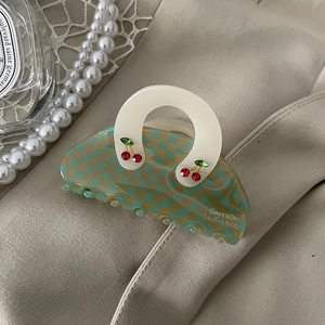 Detail of green checkerboard claw clip with red cherry accents on a luxury fabric background