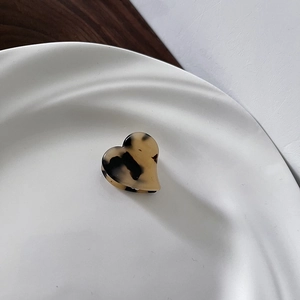 Detail view of mini heart-shaped tortoiseshell acetate hair claw on white ceramic tray