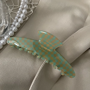 Close-up of green checkered acetate hair claw clip with side engraving on satin fabric