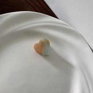 Close-up of heart-shaped mini hair claw clip with orange and teal marble texture