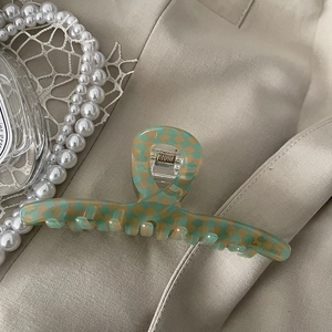 Detail of green checkerboard acetate claw clip with gold spring on a retro fabric