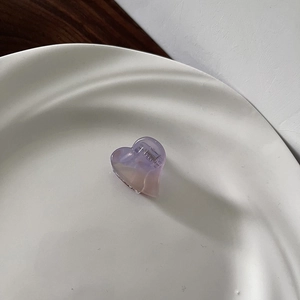 Detailed view of mini heart-shaped purple acetate hair claw clip on a white ceramic plate