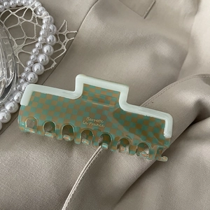 Detailed shot of green checkerboard acetate hair claw on beige fabric with pearls