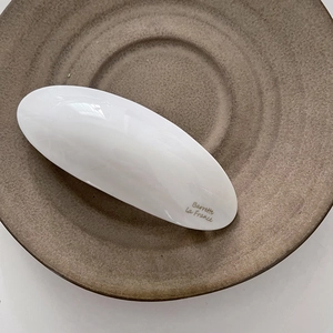 Détail d'une barrette à cheveux en résine blanche avec logo doré sur céramique