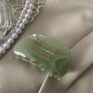 Detailed macro shot of green checkerboard acetate hair claw with golden Barrette text