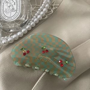 Detail of checkered acetate hair claw with cherry rhinestones on luxury silk background