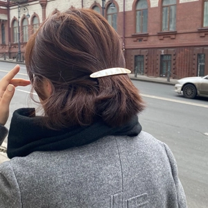 Elegant pearl white resin hair clip styled on wavy brown hair with urban city background