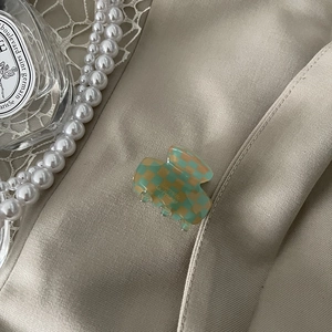 Macro detail of checkered acetate hair claw clip on elegant beige satin with pearls