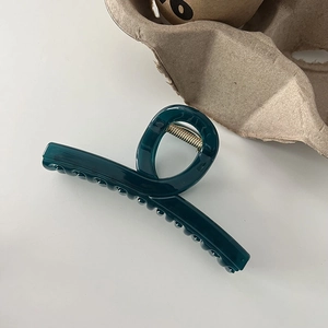 Macro view of a large dark green glossy hair claw clip with golden metal spring
