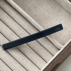 Detailed macro view of high-gloss navy resin hair barrette with gold French lettering