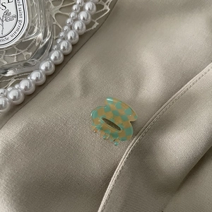 Detail of small green checkered acetate hair claw clip on silk with pearl accents