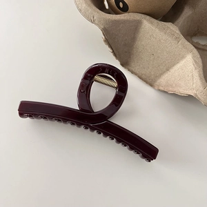 Detail of dark burgundy glossy hair claw clip with golden metal spring and smooth finish