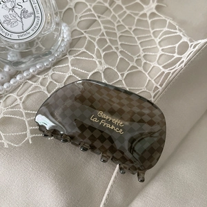 Detailed view of checkered acetate hair claw with gold script on a soft fabric backdrop