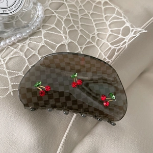 Detail of checkered hair claw clip with crystal cherry accents on tweed background