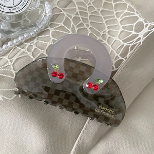 Close-up of grey checkered hair claw with crystal cherry and golden lettering