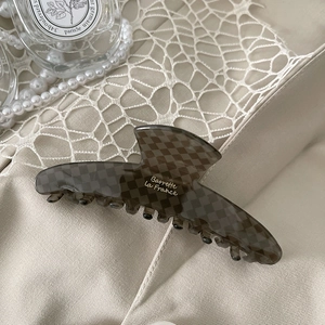 Detail view of a brown checkerboard acetate hair claw clip with gold cursive lettering