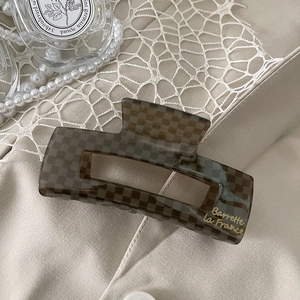 Close-up of a brown checkerboard acetate hair claw with gold lettering on beige fabric