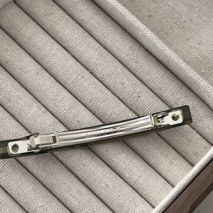 Detail showing the metal spring clip mechanism and engraved lettering on green hair barrette