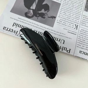 Detailed close-up of glossy black acetate hair claw clip with golden handmade inscription