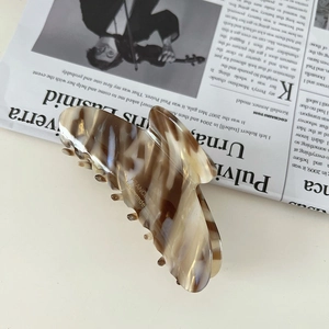 Macro shot of large acetate butterfly hair claw with marble pattern and gold logo