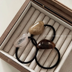 Close-up of minimalist resin bean hair ties in a wooden display box with soft lining