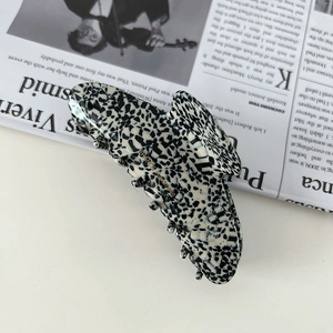 Detail of handmade acetate hair claw clip with black and white marble pattern and gold logo