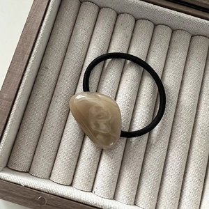Close-up of a marbled acrylic bead hair tie resting in a premium velvet jewelry tray