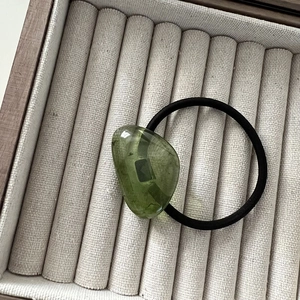 Macro detail of a translucent green bean-shaped resin bead on a black elastic hair tie