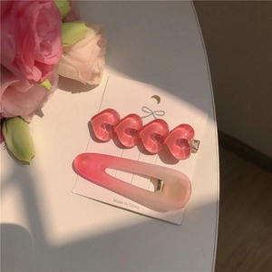 Set mit zwei rosa Herz-Haarspangen aus Harz auf einer weißen Karte mit Blumendekor