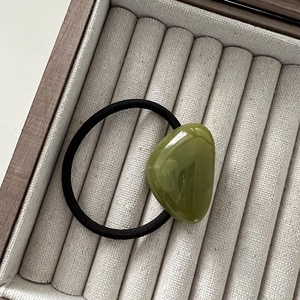 Detailed shot of an olive green pebble bead on a minimalist elastic hair tie on a velvet tray