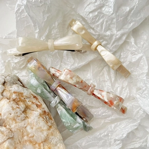 Elegant acetate bow hair clips in marble patterns displayed on a natural stone base